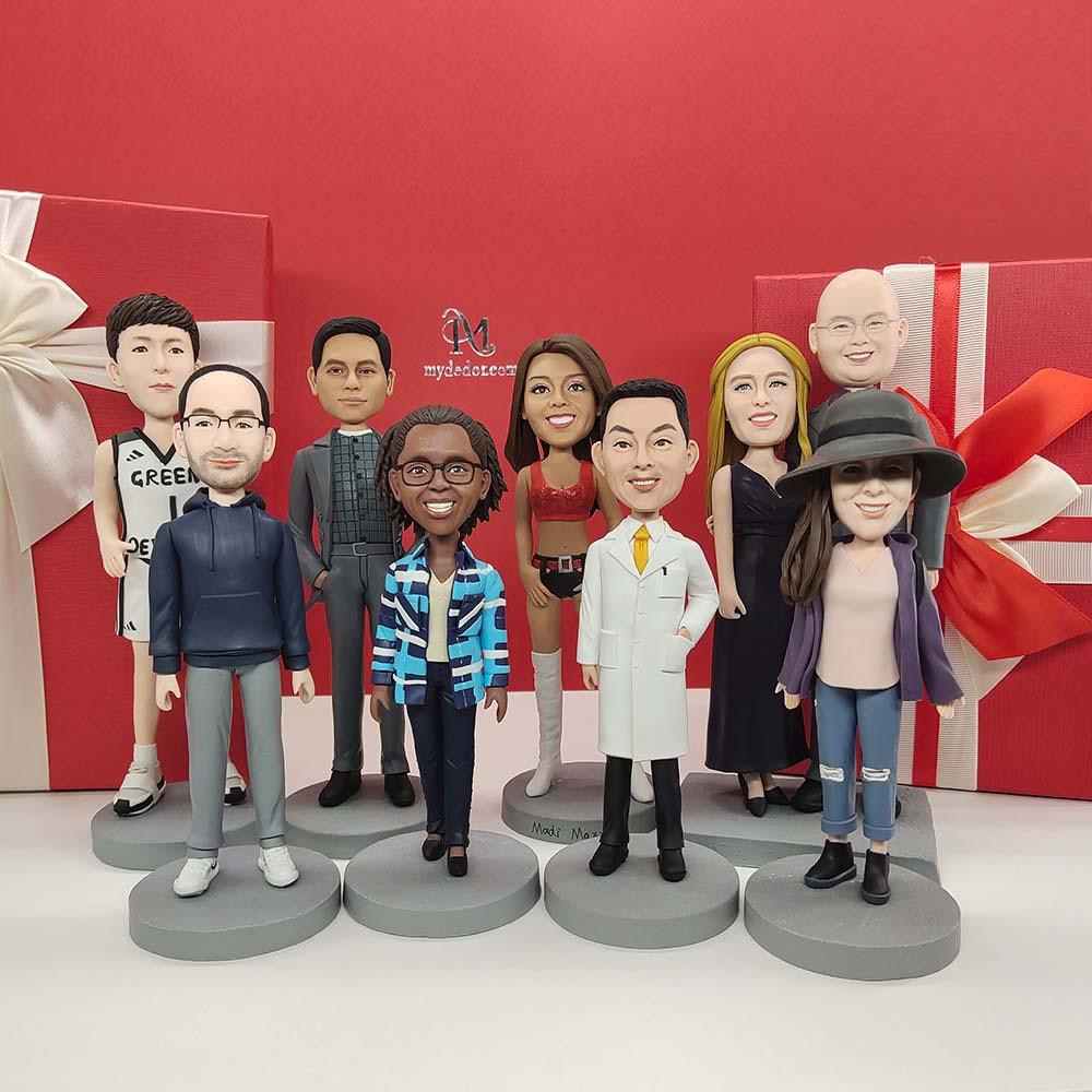 Custom handmade bobblehead figurines of diverse people in front of red gift boxes